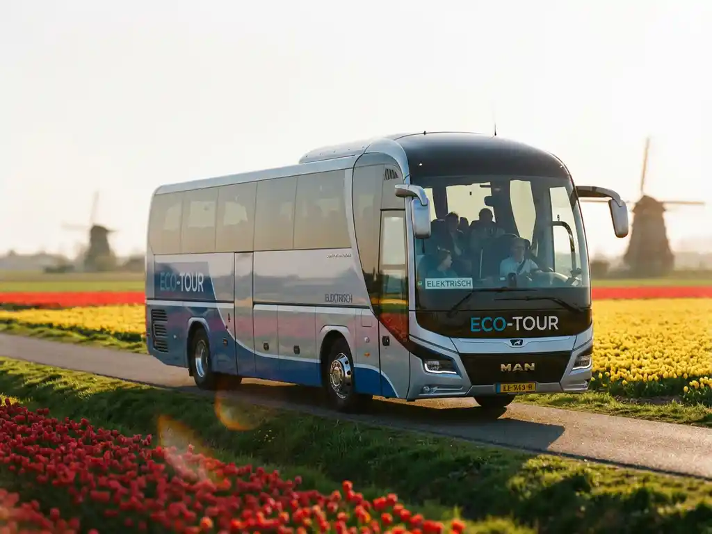 Moderne elektrische touringcar rijdt door Nederlands landschap met windmolens en tulpenvelden bij zonsondergang