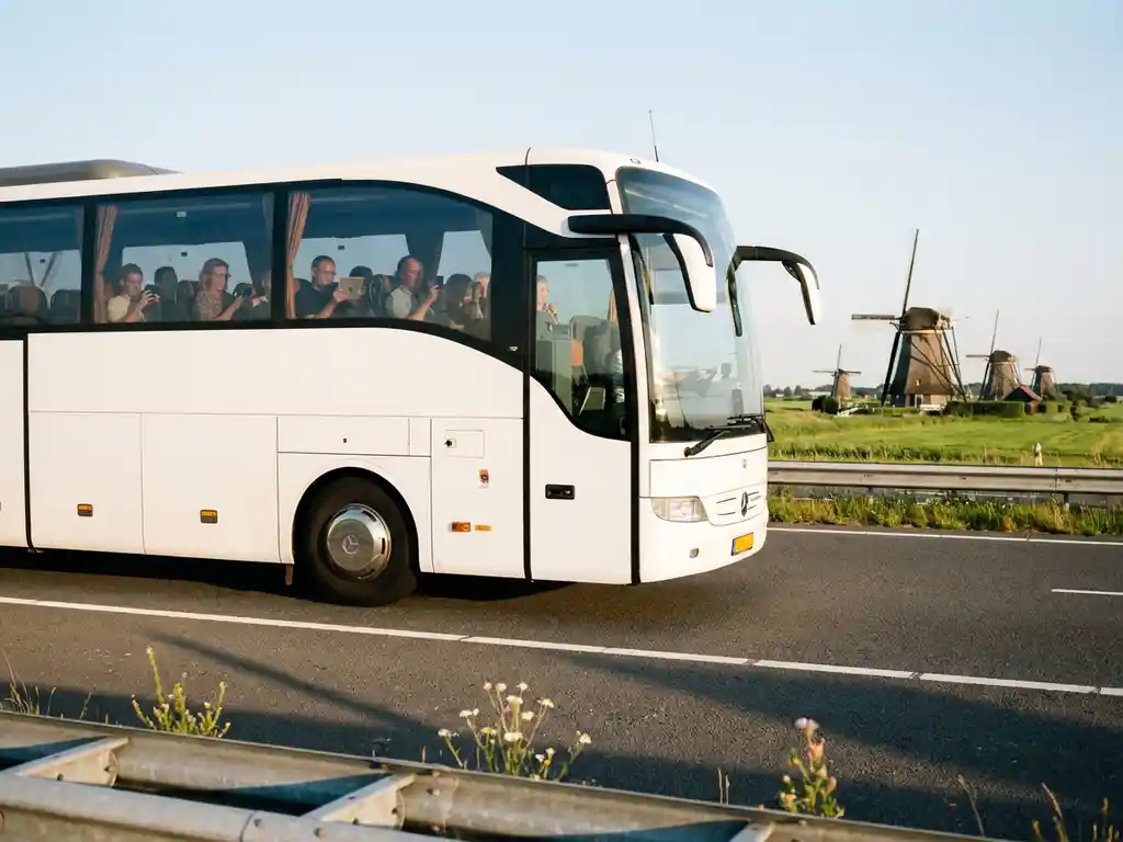 Witte touringcar rijdt over Nederlandse snelweg met windmolens en groene polders op de achtergrond