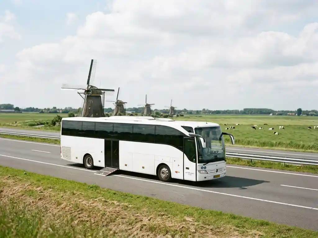 Witte toegankelijke touringcar met rolstoellift rijdt over Nederlandse snelweg langs windmolens en groene polders