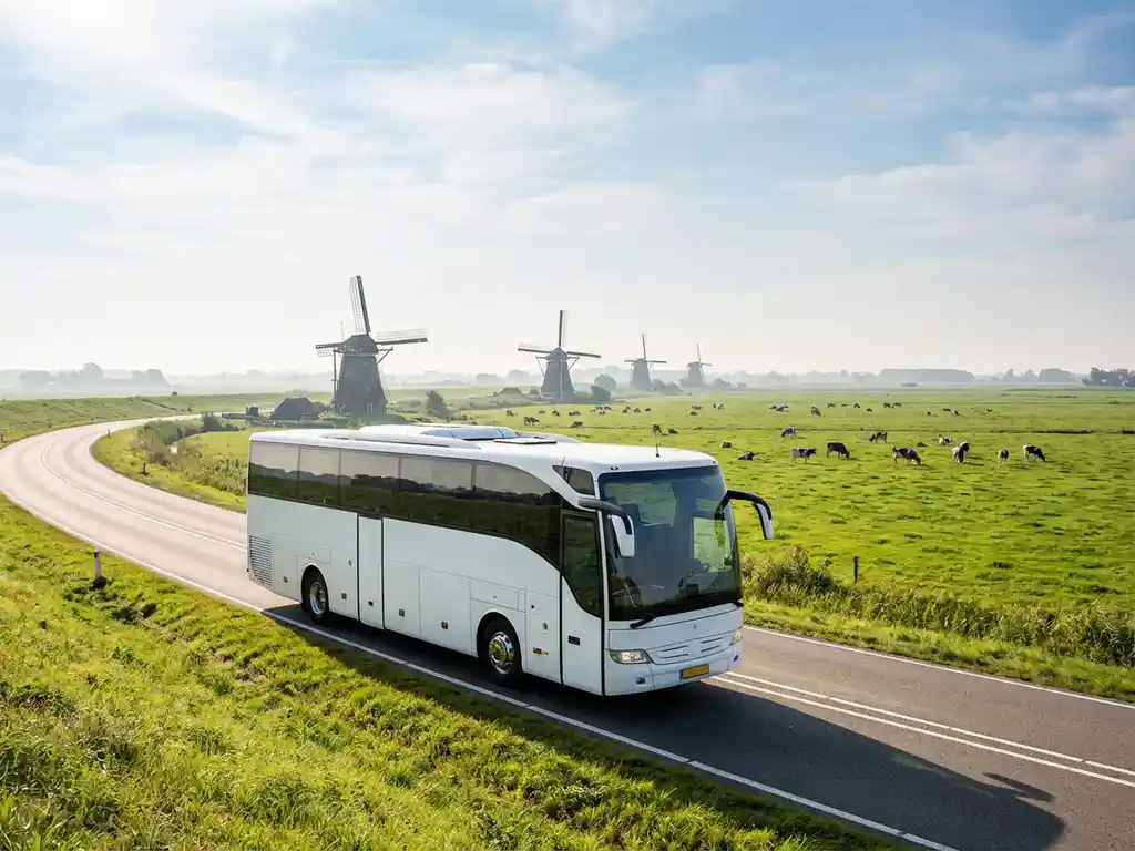 Witte touringcar rijdt door Nederlands platteland met groene velden en traditionele windmolens op de achtergrond