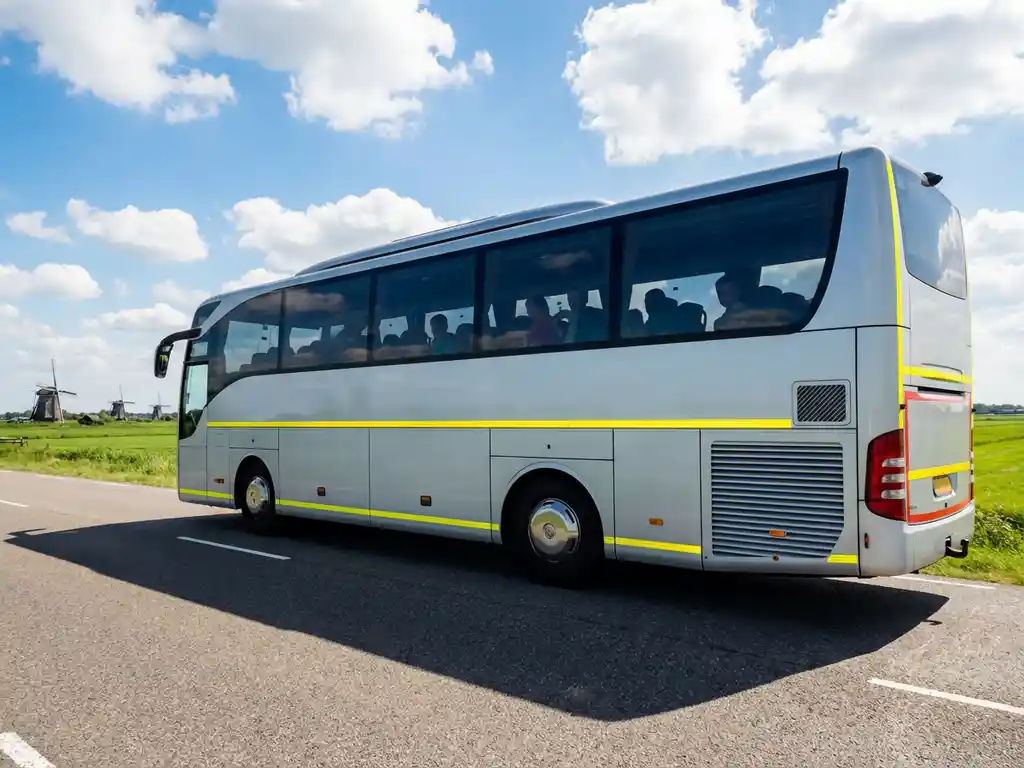 Witte touringcar met kinderen rijdt over Nederlandse snelweg langs traditionele windmolens en groene polders