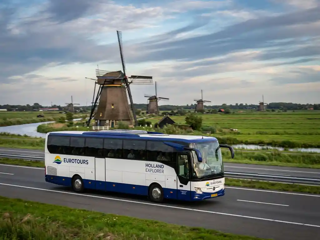 Moderne touringcar rijdt over Nederlandse snelweg met traditionele windmolens en groene polders op de achtergrond