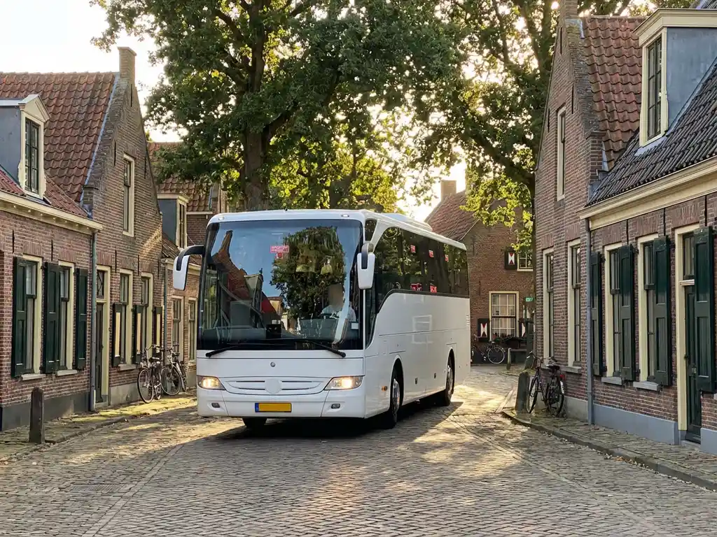 Witte touringcar rijdt door Nederlandse dorpsstraat met bakstenen huizen, rode dakpannen en kasseien
