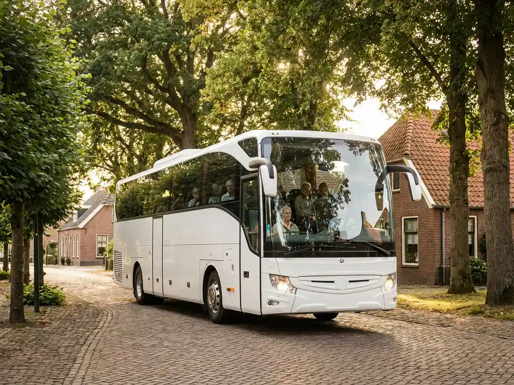 Witte touringcar rijdt door Nederlands dorp met traditionele bakstenen huizen en rode pannendaken onder schaduwrijke bomen