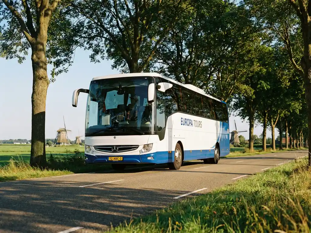 Witte en blauwe touringcar rijdt door Nederlands landschap met traditionele windmolens en groene polders
