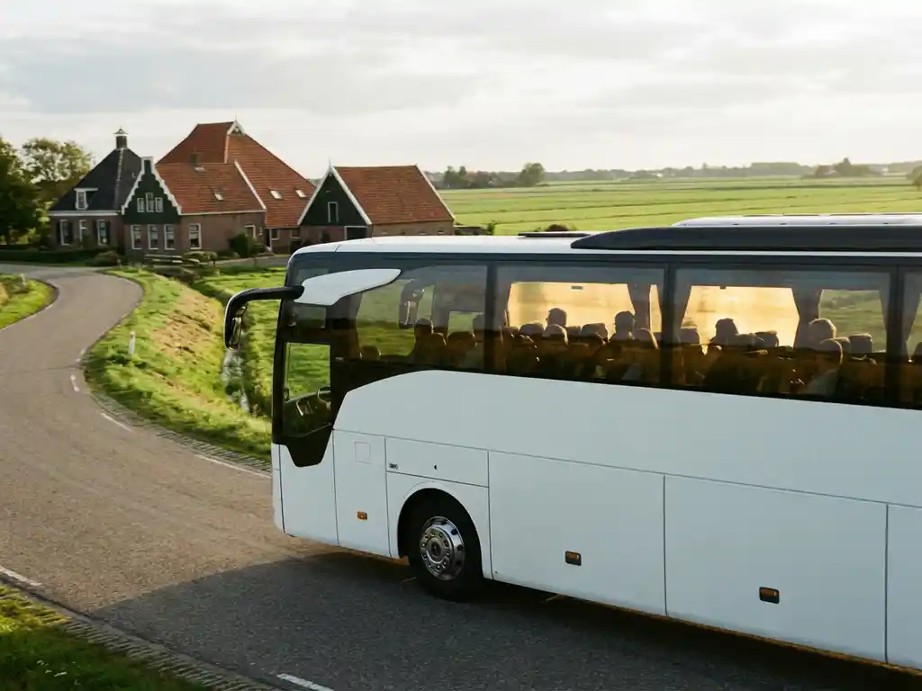 Witte touringcar rijdt door Nederlands landschap met rode boerderijen en groene polders in gouden middaglicht