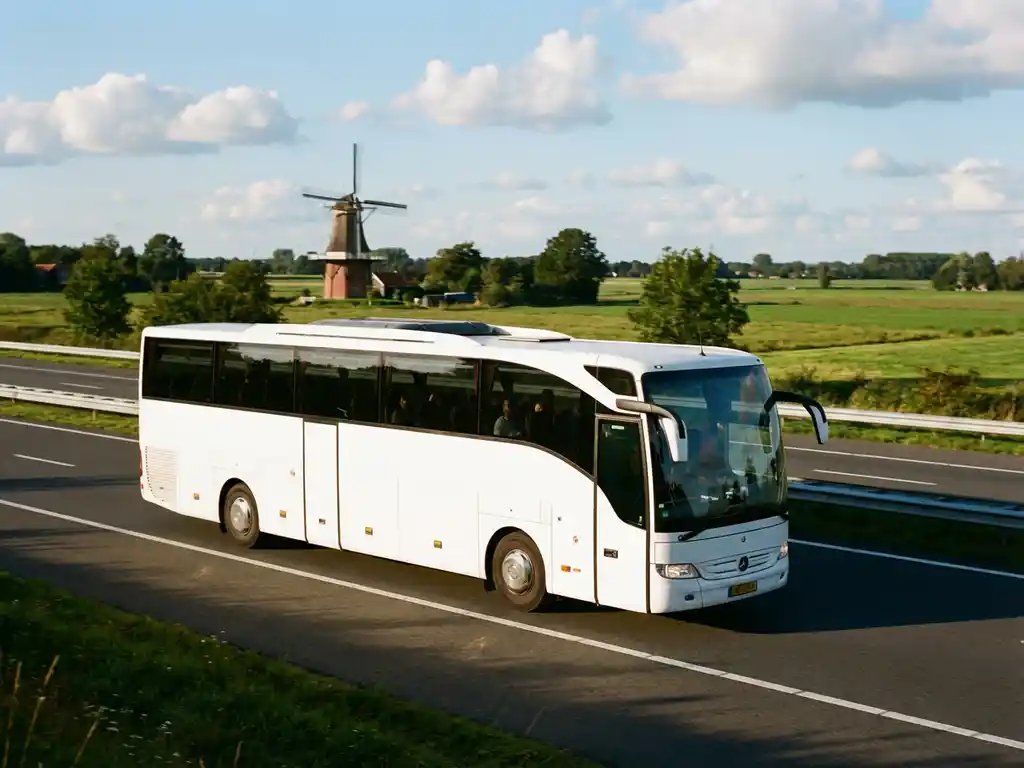 Witte touringcar rijdt over Nederlandse snelweg met traditionele rode bakstenen windmolen in groene landschap