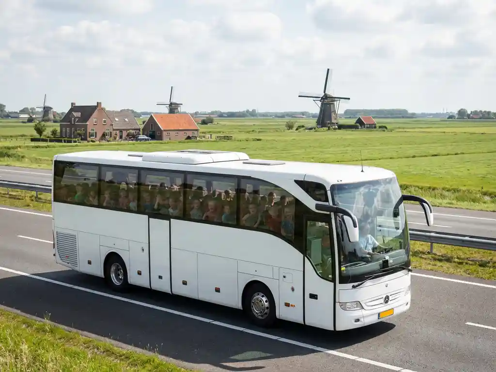 Witte touringcar met schoolkinderen rijdt over Nederlandse snelweg met windmolens en polders op achtergrond