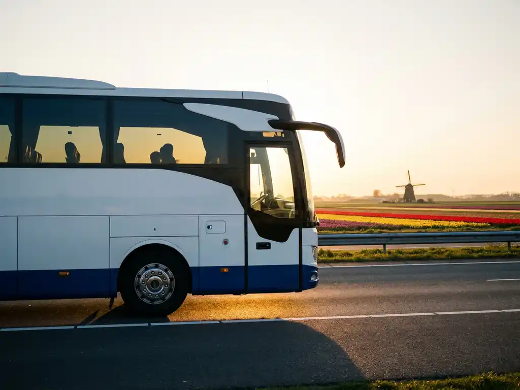 Elektrische touringcar op Nederlandse snelweg langs tulpenvelden en windmolen, laadpoort zichtbaar, warm middaglicht.