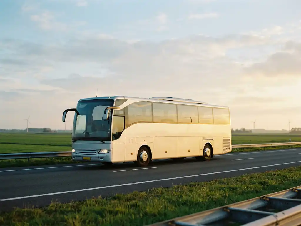 Moderne touringcar rijdt over Nederlandse snelweg langs groene polders, met vage windmolens en gouden middagzon op de witte carrosserie.