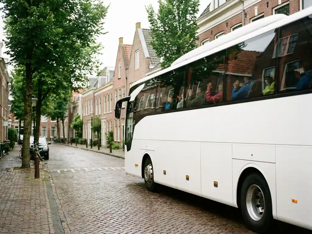 Moderne touringcar met festivalgangers rijdt door een Nederlandse dorpsstraat met bakstenen huizen en groene bomen.