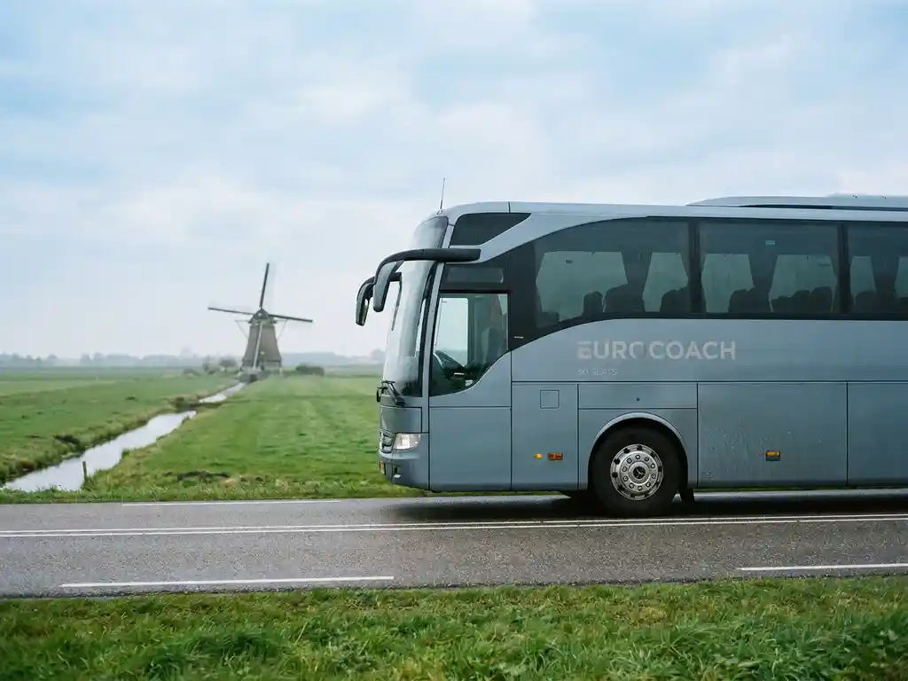 Moderne touringcar voor 50 passagiers rijdt over een Nederlandse polderwegen met groene weilanden en molen op de achtergrond.