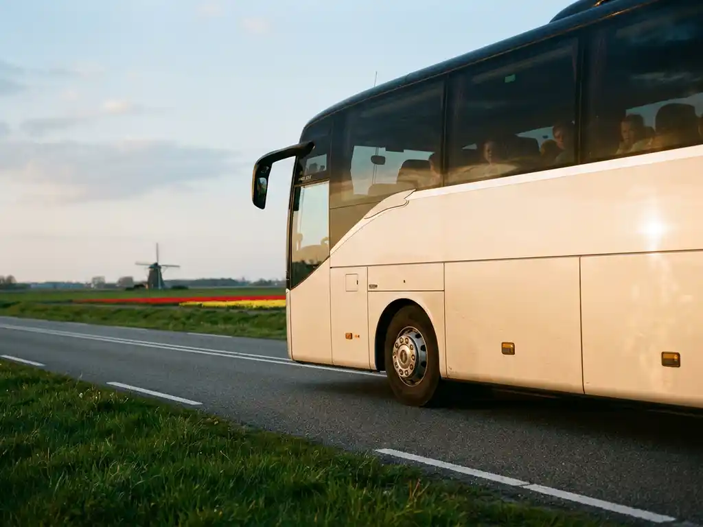 Moderne touringcar met schoolkinderen rijdt door Nederlands polderlandschap met tulpenvelden en windmolen op de achtergrond.