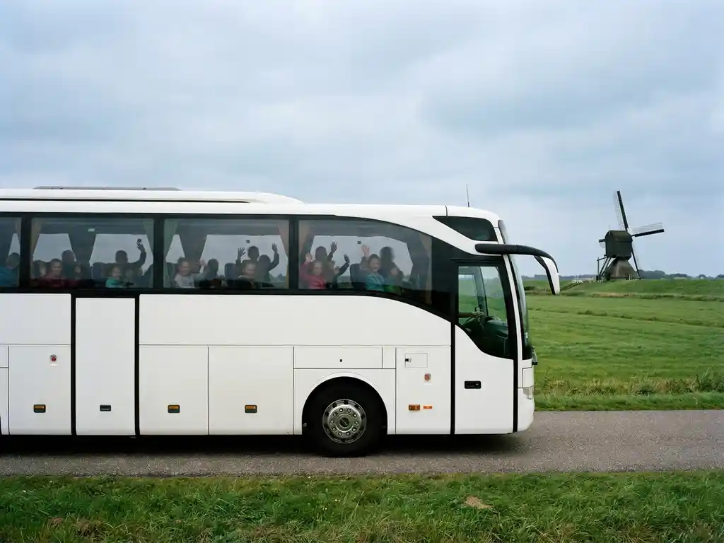 Moderne touringcar met schoolkinderen op een Nederlandse polderwegen, met groene weilanden en een windmolen op de achtergrond.