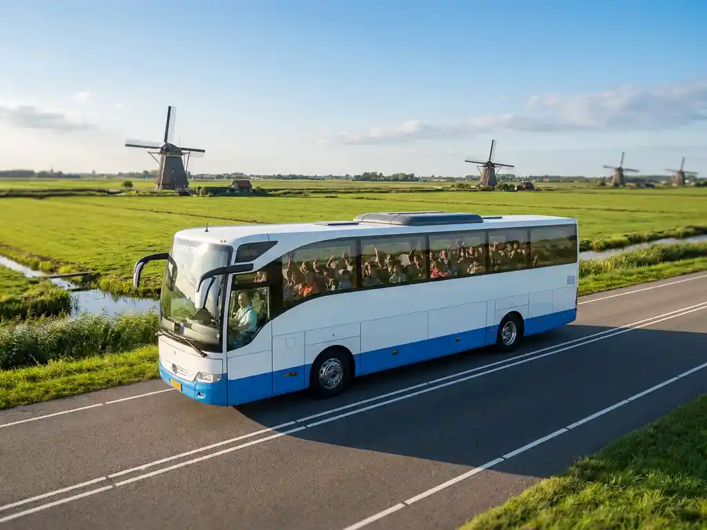 Touringcar met schoolkinderen rijdt door een Hollands polderlandschap met windmolens en groene weilanden onder een blauwe lucht.