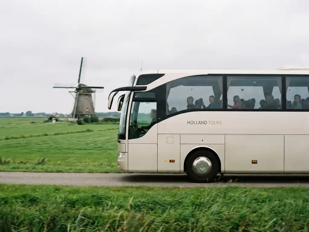 Moderne touringcar met schoolkinderen op een Nederlandse polderwegen, groene weilanden en een windmolen op de achtergrond.