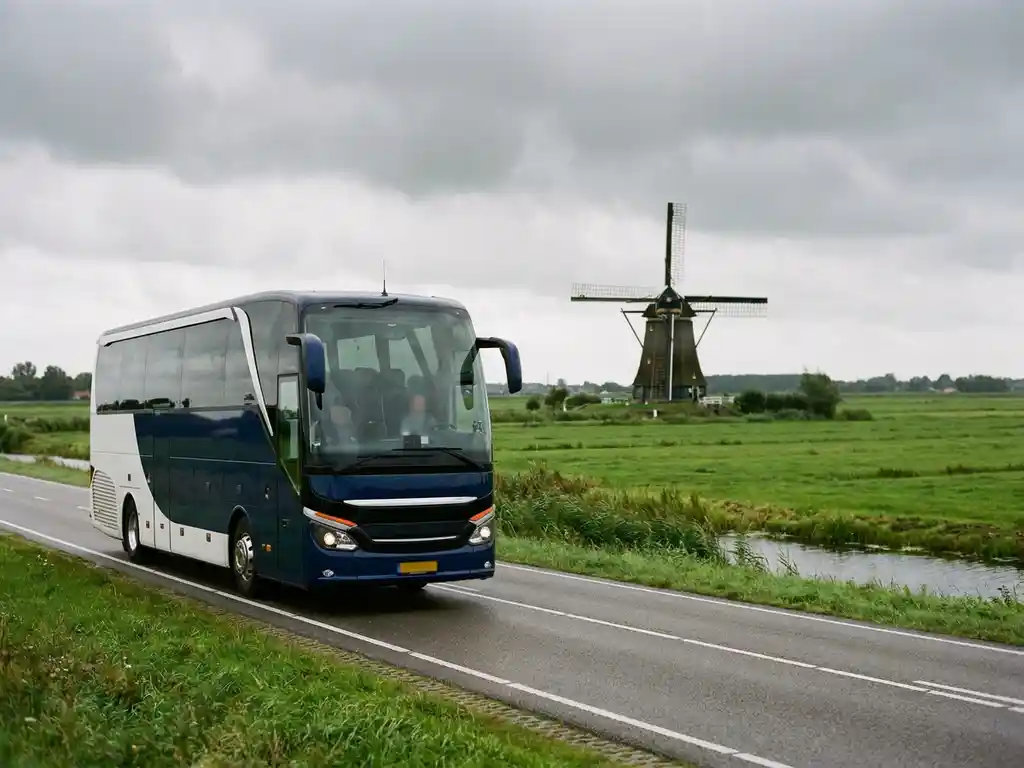 Moderne touringcar rijdt door een Hollands polderlandschap met groene weiden en een traditionele windmolen op de achtergrond.