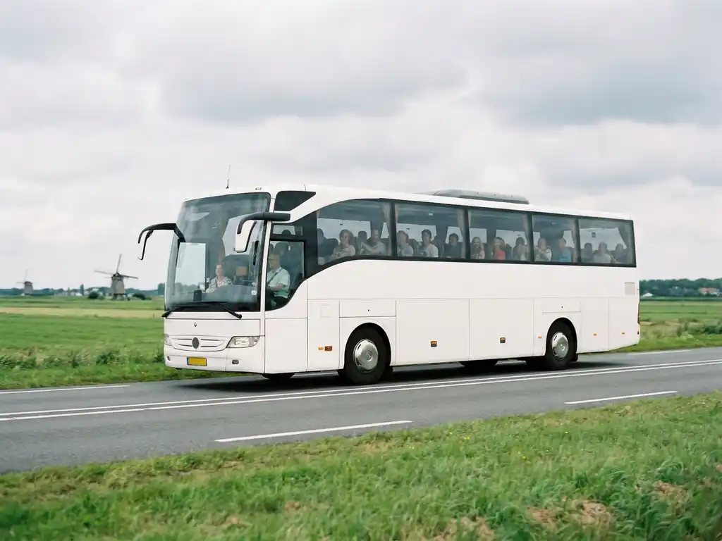 Moderne touringcar rijdt over Nederlandse snelweg door vlak polderlandschap met windmolens op de achtergrond.