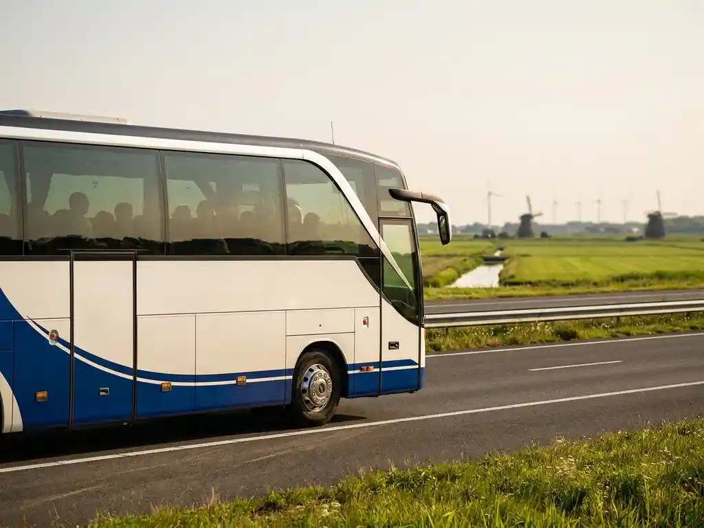 Moderne touringcar rijdt over Nederlandse snelweg door vlak polderlandschap met windmolens op de achtergrond.