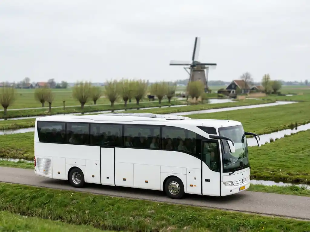 Moderne touringcar voor 50 personen rijdt over een Nederlandse polderwegen met groene weilanden en een molen op de achtergrond.