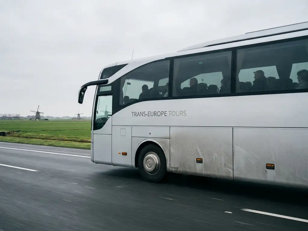 Moderne touringcar met passagiers op Nederlandse snelweg, met groene polders en windmolens op de achtergrond.