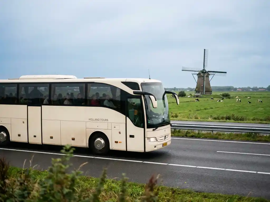 Touringcar met 50 passagiers op Nederlandse snelweg, met groene polders en traditionele windmolen op de achtergrond.