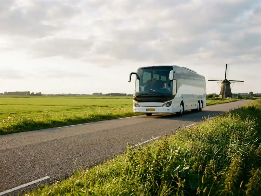 Moderne touringcar op een Nederlandse polderwegen met groene weilanden, windmolen op achtergrond en warm middaglicht.