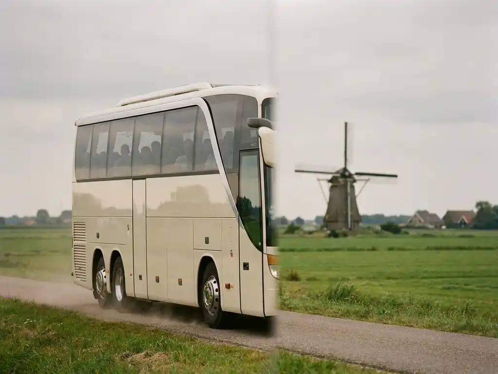Moderne touringcar rijdt over een Nederlandse polderwegen met groene weilanden en een molen op de achtergrond.