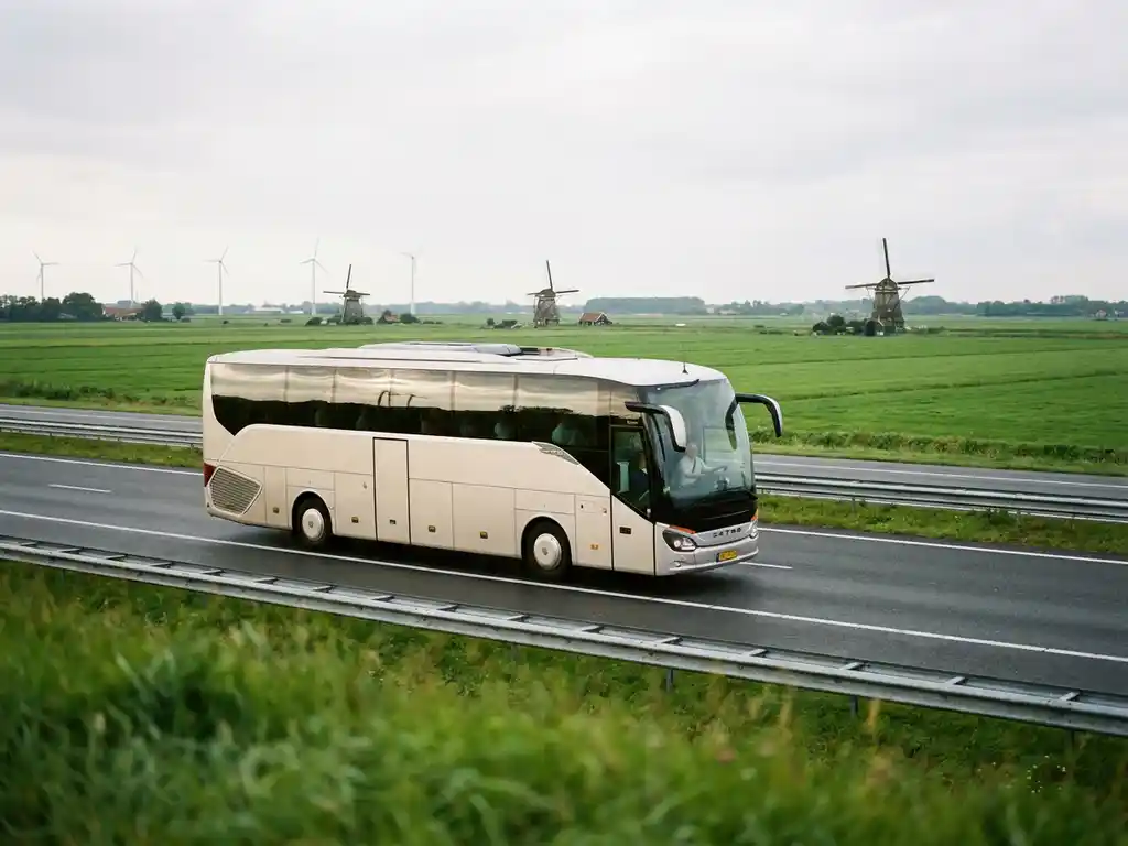 Moderne touringcar rijdt over Nederlandse polderwegen met windmolens en groene weilanden op de achtergrond.