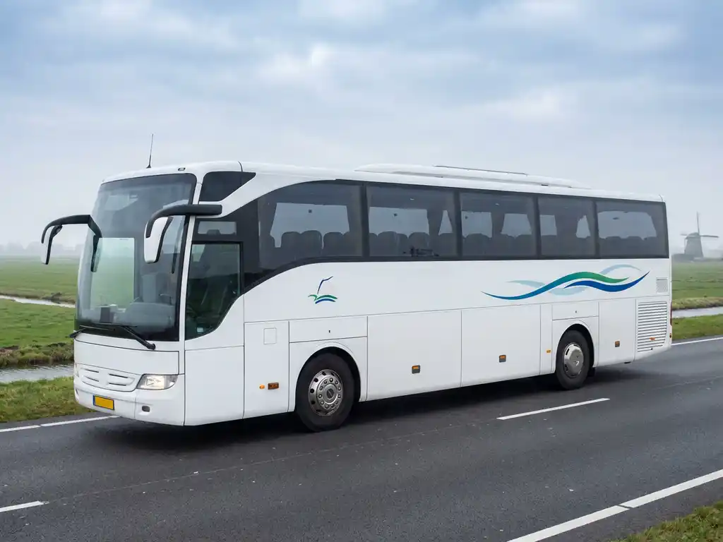 Witte touringcar op Nederlandse snelweg met polderlandschap en windmolen op de achtergrond onder bewolkte lucht.