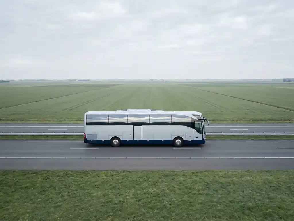 Moderne touringcar rijdt over rechte Nederlandse snelweg, omgeven door vlakke groene polders onder een bewolkte lucht.