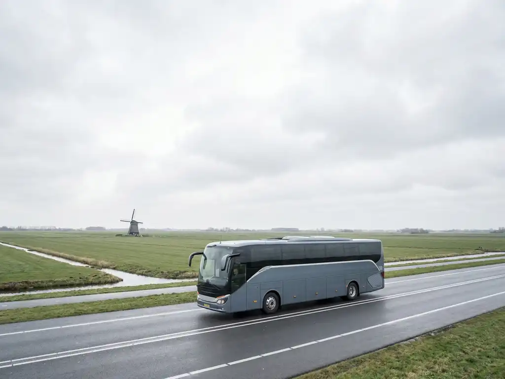 Moderne touringcar op Nederlandse snelweg met vlak polderlandschap, molen in de verte en bewolkte lucht.