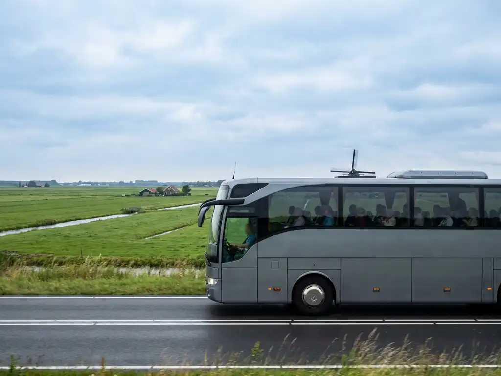 Touringcar rijdt over Nederlandse snelweg door groen polderlandschap met windmolen aan de horizon.