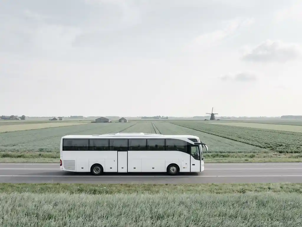 Moderne touringcar op een rechte Nederlandse snelweg, omgeven door vlak polderlandschap met een windmolen in de verte.