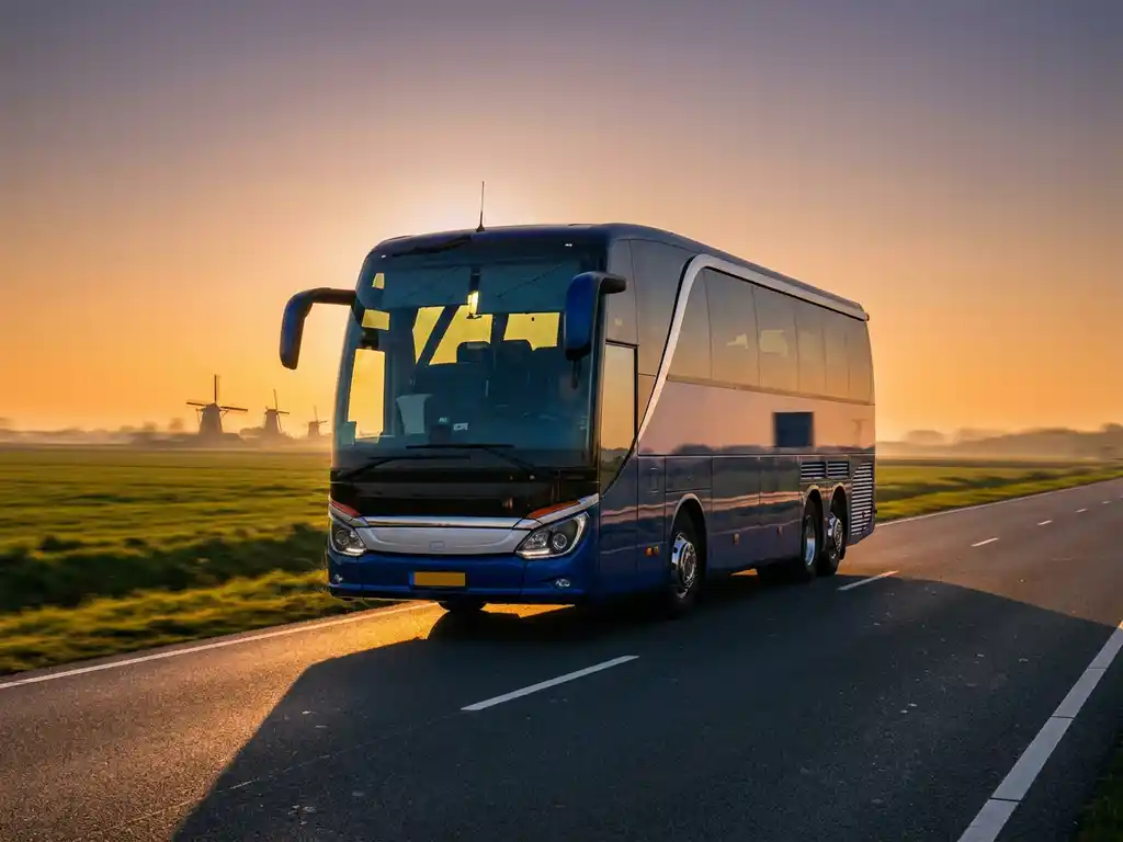 Moderne touringcar op Nederlandse snelweg met polders en windmolens op de achtergrond in gouden middaglicht.