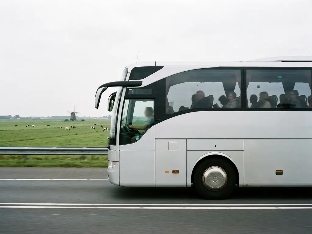 Touringcar rijdt over Nederlandse snelweg met polderlandschap, windmolen en bewolkte lucht op de achtergrond.