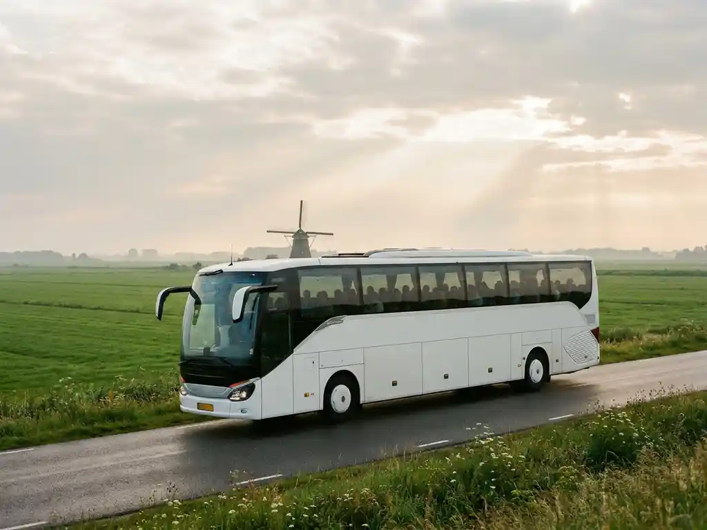 Moderne touringcar op een Nederlandse polderwegweg, omgeven door groene weilanden, traditionele molen en bewolkte lucht op de achtergrond.
