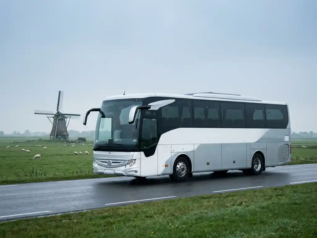 Moderne touringcar voor 50 personen rijdt over een Nederlandse polderwegen met weilanden en een windmolen op de achtergrond.