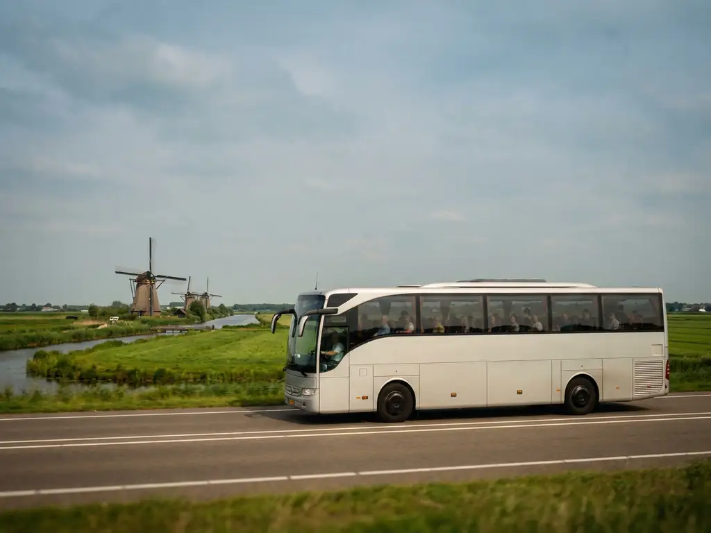 Moderne touringcar rijdt door een Hollands polderlandschap met windmolens en groene weilanden op de achtergrond.
