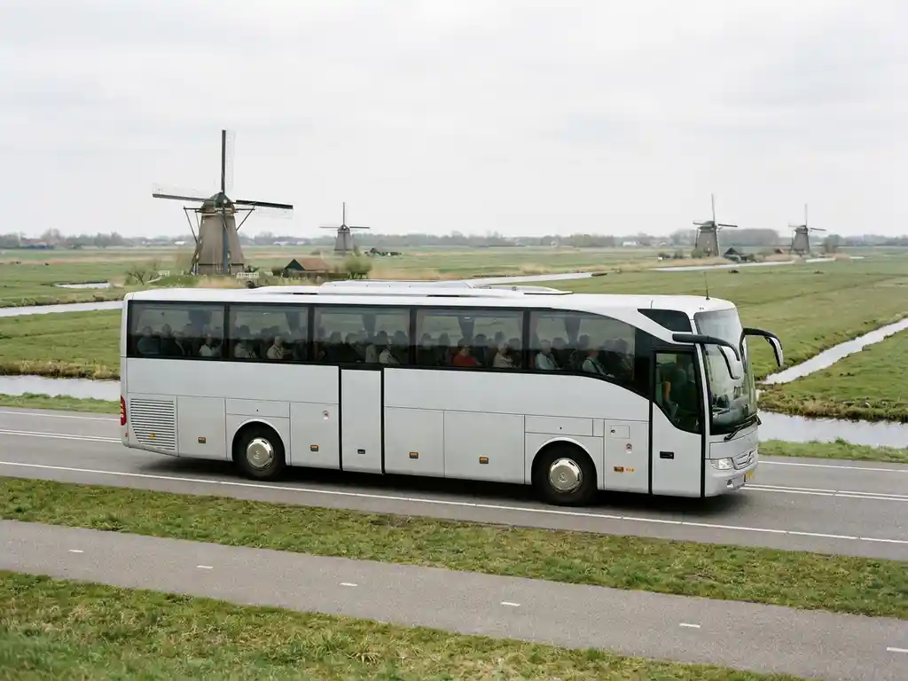 Touringcar rijdt door typisch Nederlands polderlandschap met windmolens en groene weilanden onder bewolkte lucht.