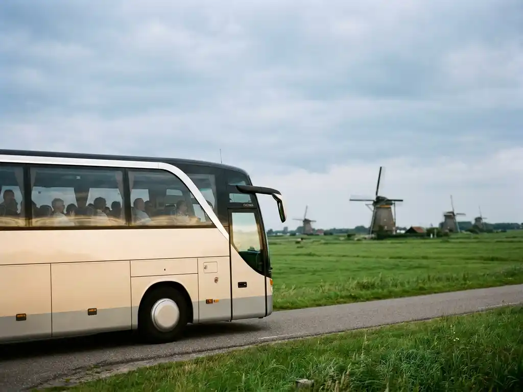 Touringcar rijdt over een Nederlandse polderwegweg met windmolens en groene weilanden op de achtergrond.