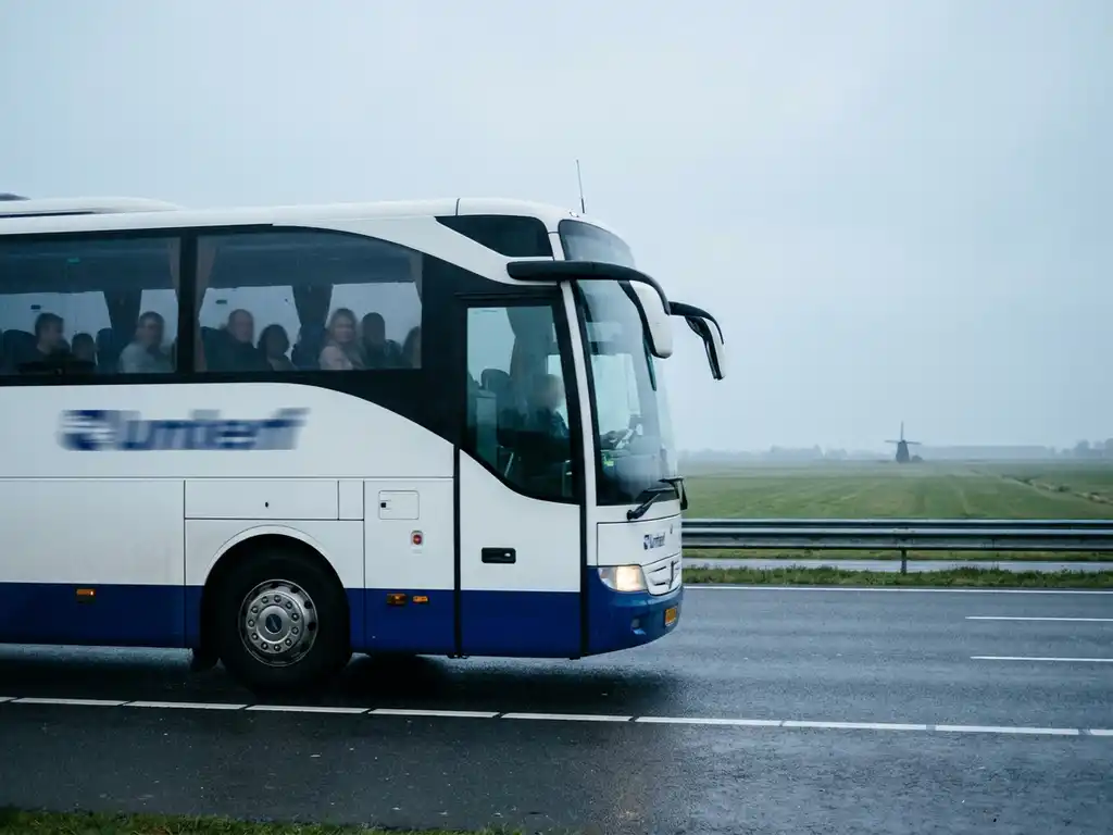 Touringcar rijdt over Nederlandse snelweg met polderlandschap en windmolen op de achtergrond.