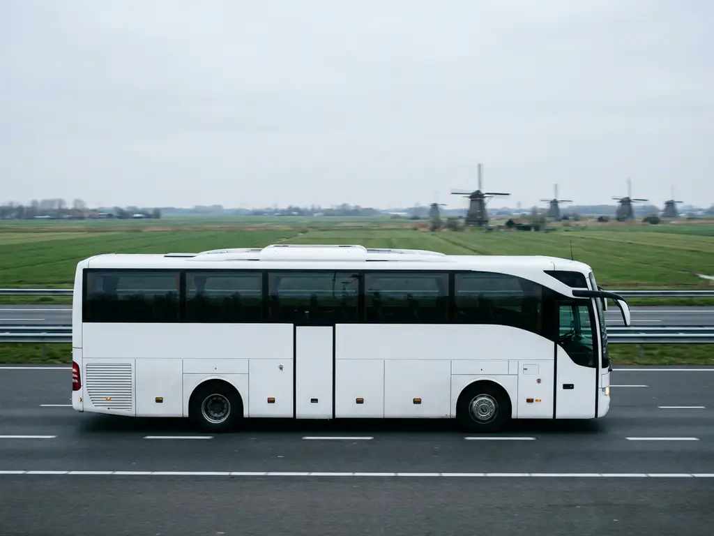 Moderne witte touringcar rijdt over Nederlandse snelweg met groene polders en windmolens op de achtergrond.