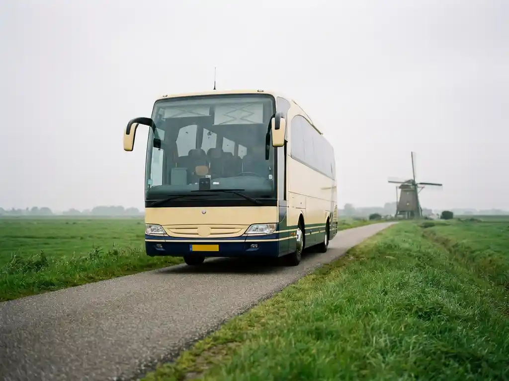 Moderne touringcar rijdt over een Nederlandse polderwegen met groene weilanden en een molen op de achtergrond.