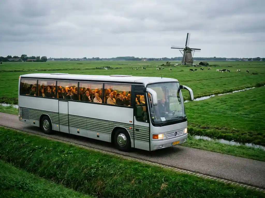 Touringcar rijdt over een polderweg in Nederland, met groene weilanden en een windmolen op de achtergrond.