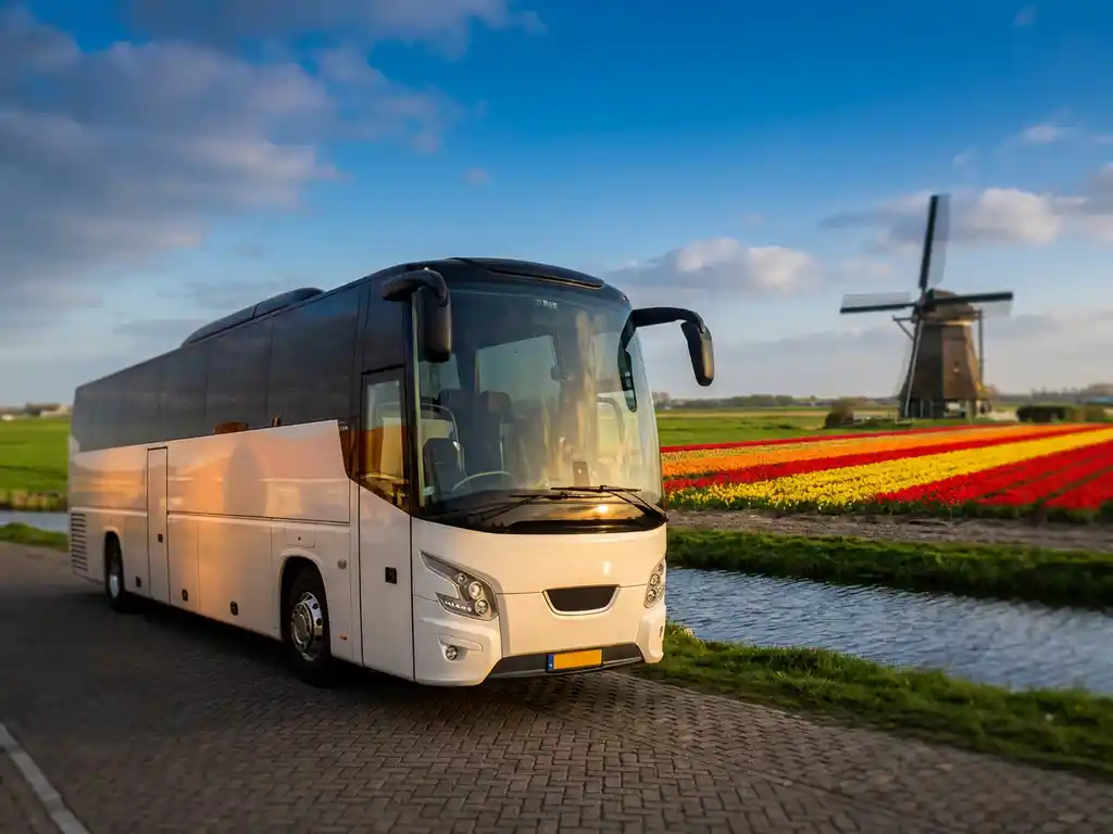 Luxe touringcar geparkeerd langs Nederlands kanaal met tulpenvelden en windmolen op de achtergrond in warm middaglicht.