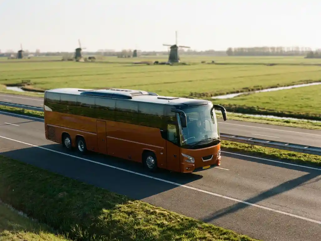 Touringcar rijdt over Nederlandse snelweg langs groene polders en windmolens in warm middaglicht.