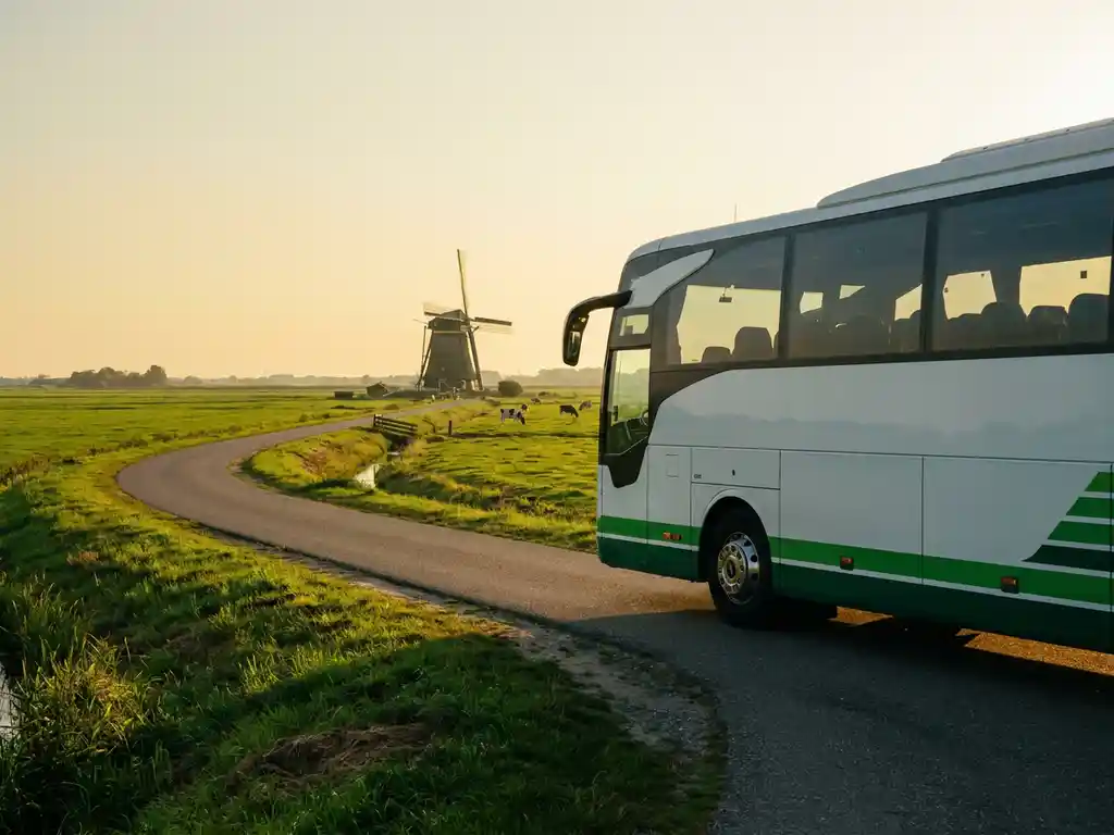 Touringcar rijdt door Nederlands polderlandschap met windmolen op de achtergrond in warm middagzonlicht.