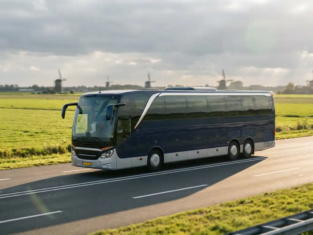 Moderne touringcar rijdt over Nederlandse snelweg langs groene weilanden en windmolens in middaglicht.