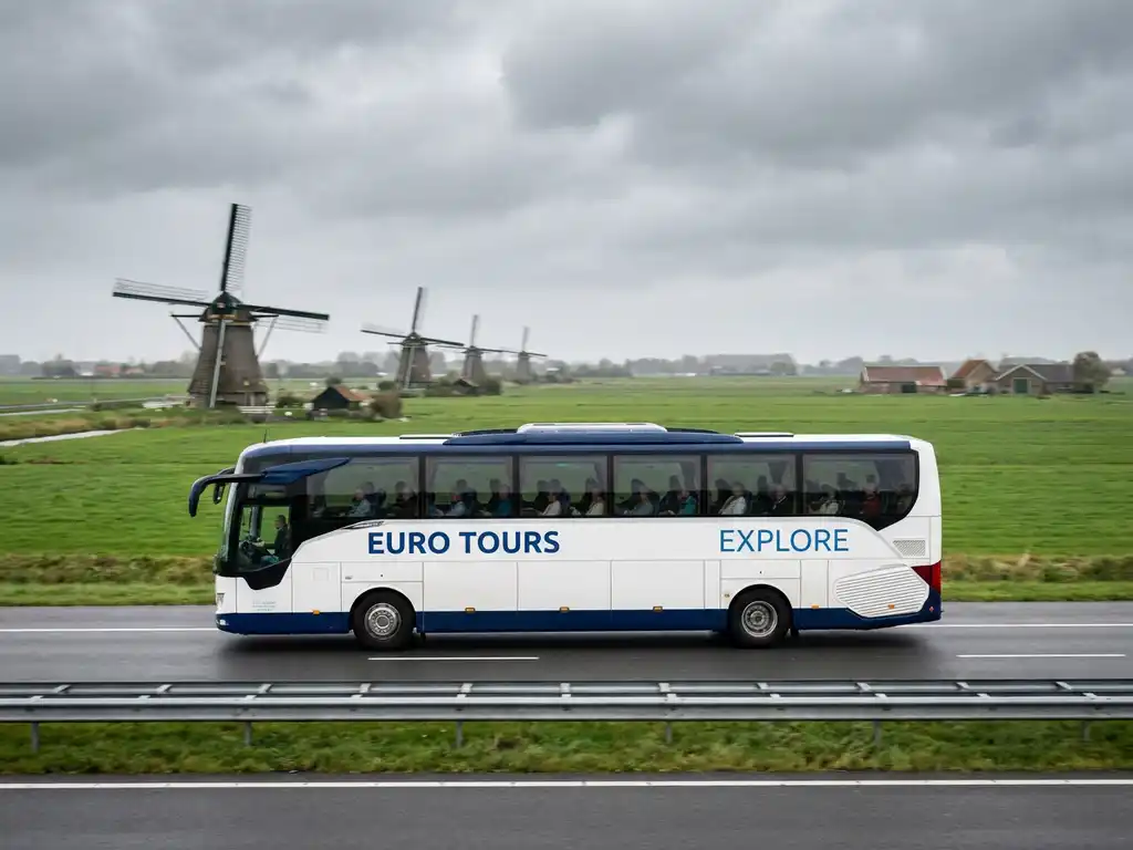 Moderne touringcar rijdt over Nederlandse snelweg met windmolens en groene polders op de achtergrond.